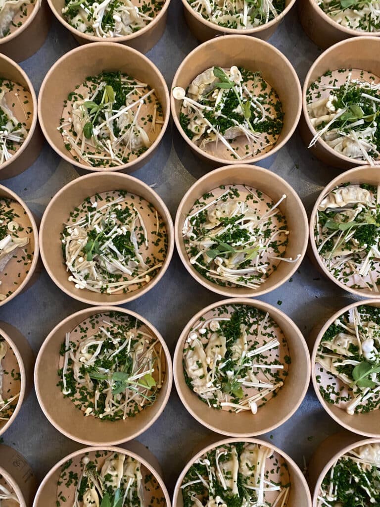 Rijen kartonnen bowls met dumplings, taugé en bieslook, klaargezet bij Gastro Henri.