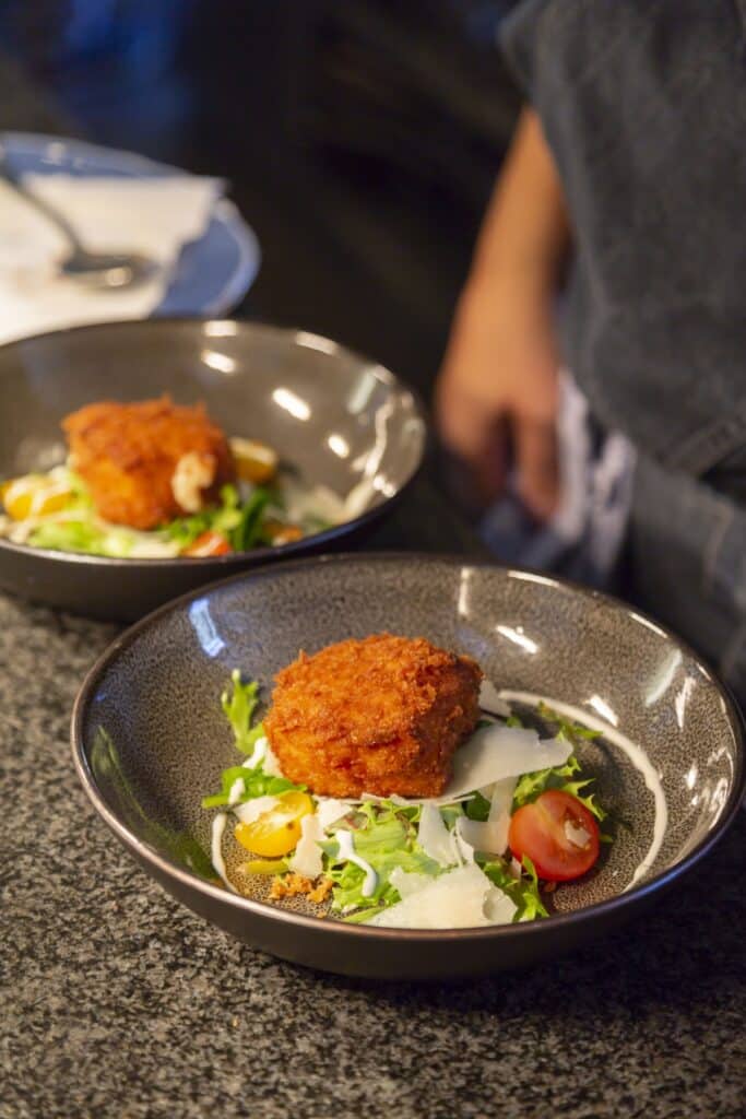Twee diepe borden met een krokante kroket op sla, tomaat en parmezaan, bij Eethuis De Steeg.