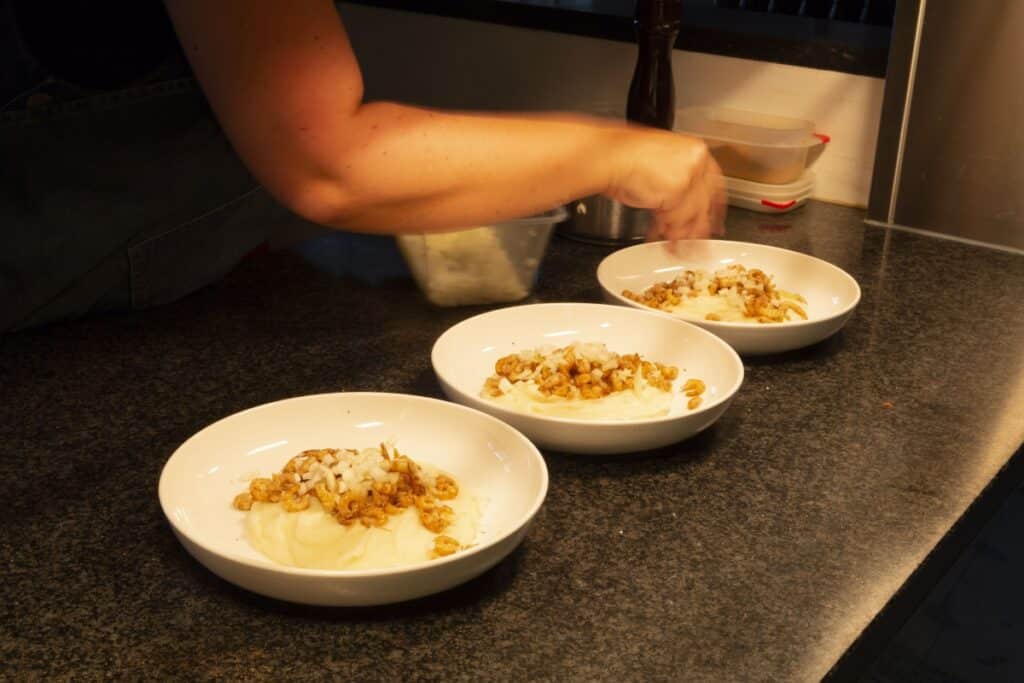 Drie borden met puree en grijze garnalen worden afgewerkt in de keuken van Eethuis De Steeg.