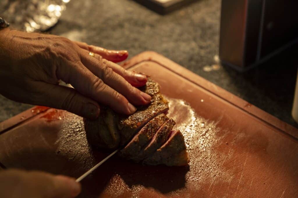 Kok snijdt een gebraden stuk vlees in plakken op een snijplank in de keuken.