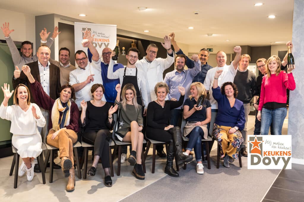 Juichende leden van GastroRSL bij een groepsfoto in de toonzaal van Dovy Keukens.