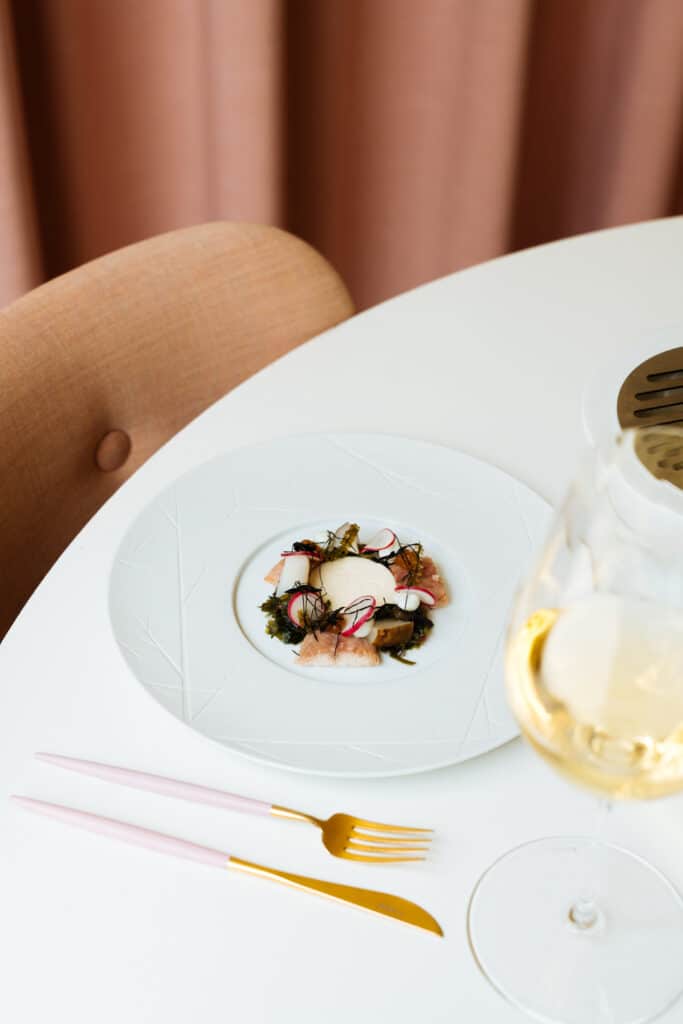 Voorgerecht bij CRKL met rauwe vis, radijs en zeewier, met een glas witte wijn.